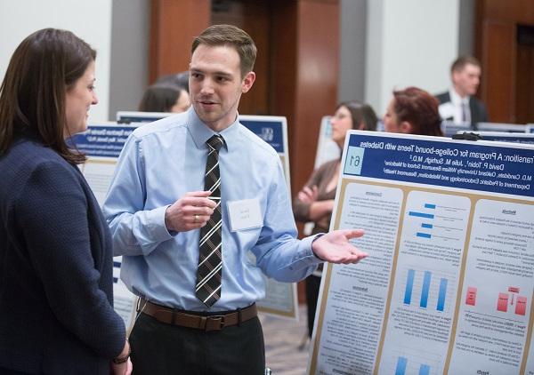 An M4 presents his research poster to a faculty member at the annual Capstone Colloquium
