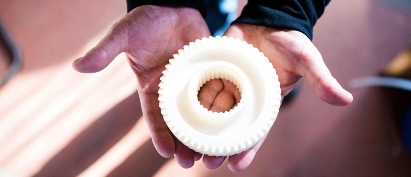 Two hands holding a round white donut shaped object with gear-like teeth around the edges.