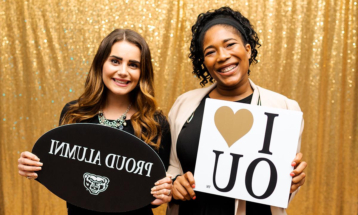 两名女子站在一起，举着写有“我爱欧大”和“自豪的校友”的标语。
