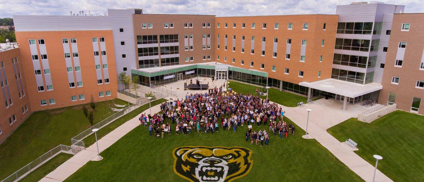 Aerial shot of large group of HC students stand on O U campus with large Grizz mascot painted on the ground