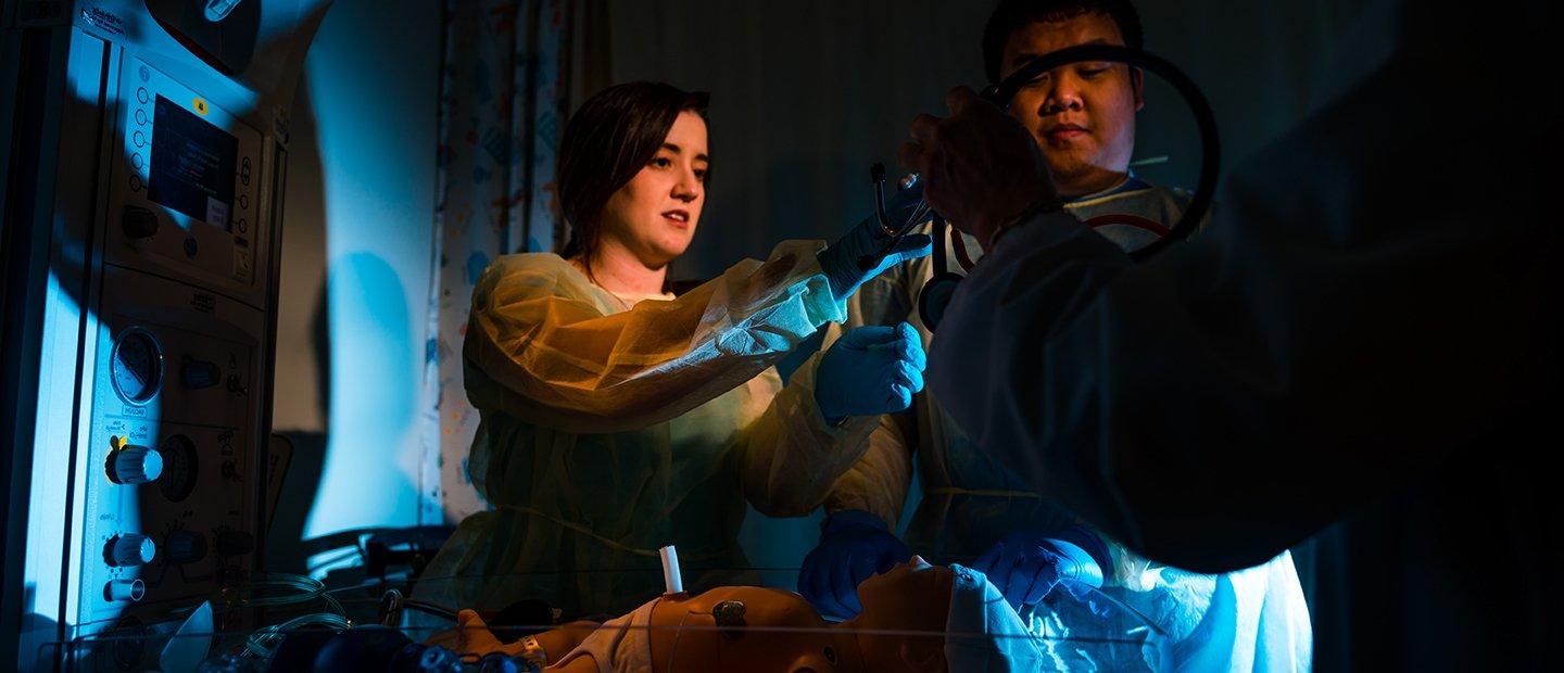 two students practicing with medical equipment in a dark room